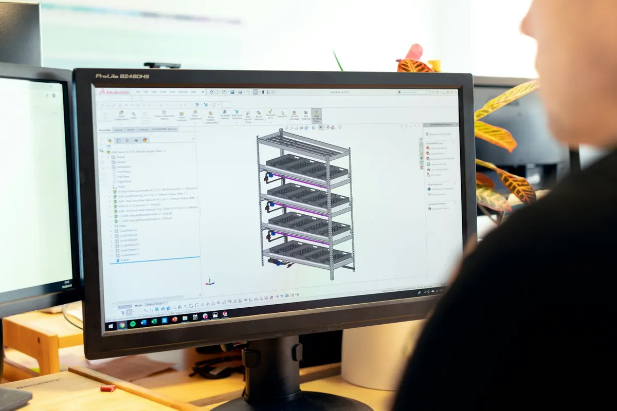 Engineer dilihat dari belakang memandangi model CAD 3D struktur rak bertingkat di layar monitor