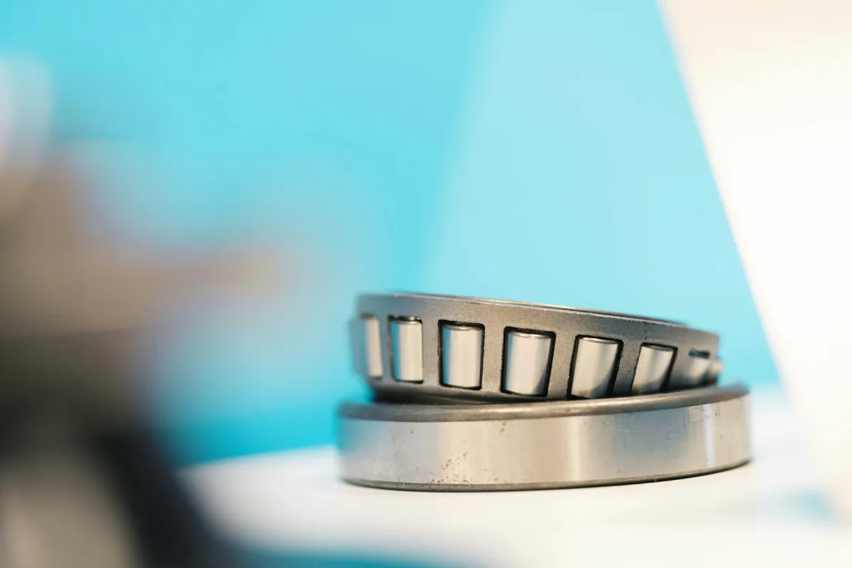 Sebuah tapered roller bearing, cincin dalam dengan rol dan cincin luarnya, tergeletak di atas permukaan dengan latar biru