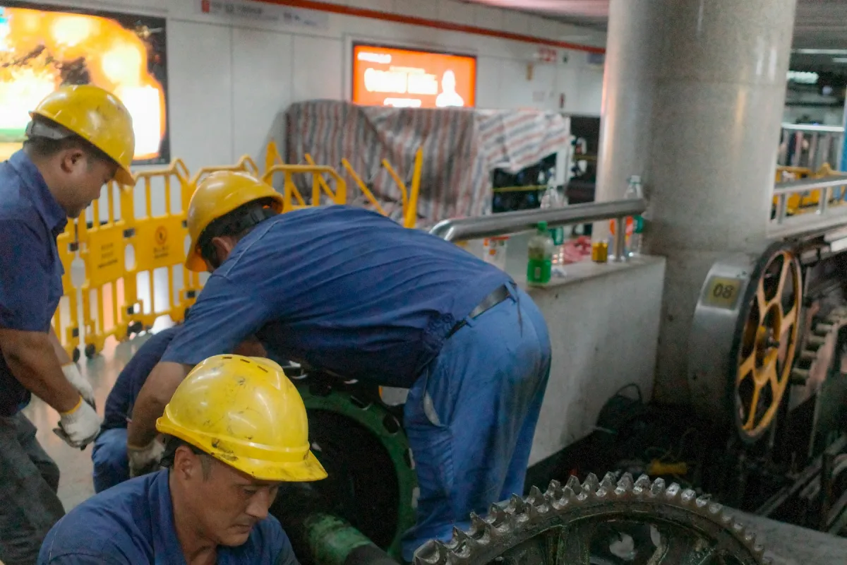 Teknisi berhelm kuning dan berseragam biru memperbaiki roda gigi besar pada mesin industri